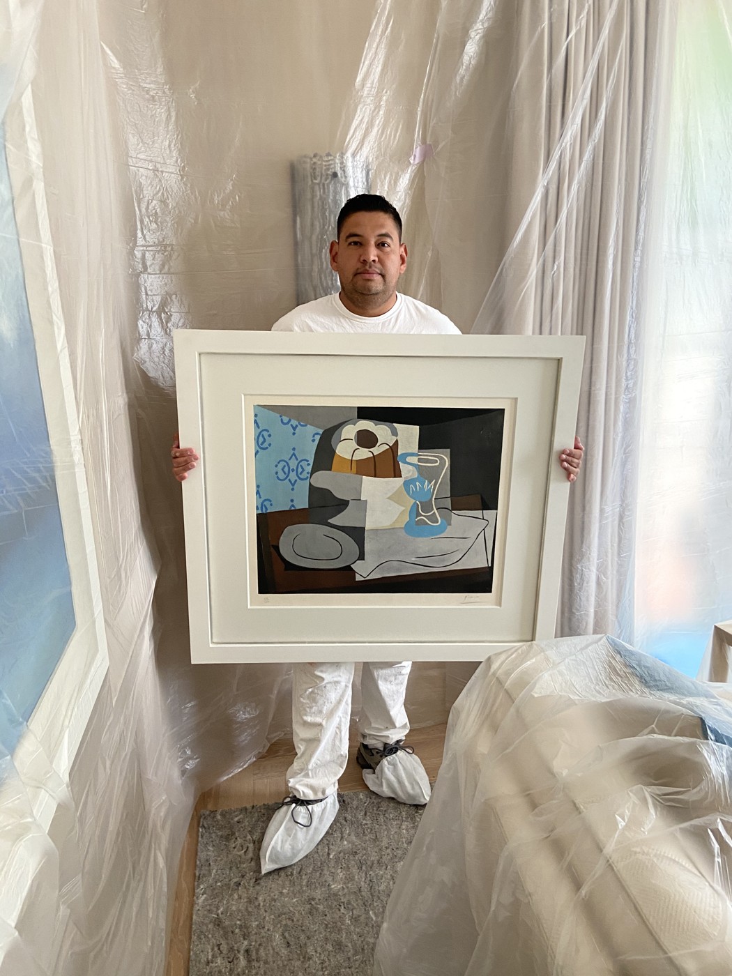 Luis Rivas in painter whites and shoe covers, working in a fully plastic-sheeted Palm Beach residence around a client's framed artwork