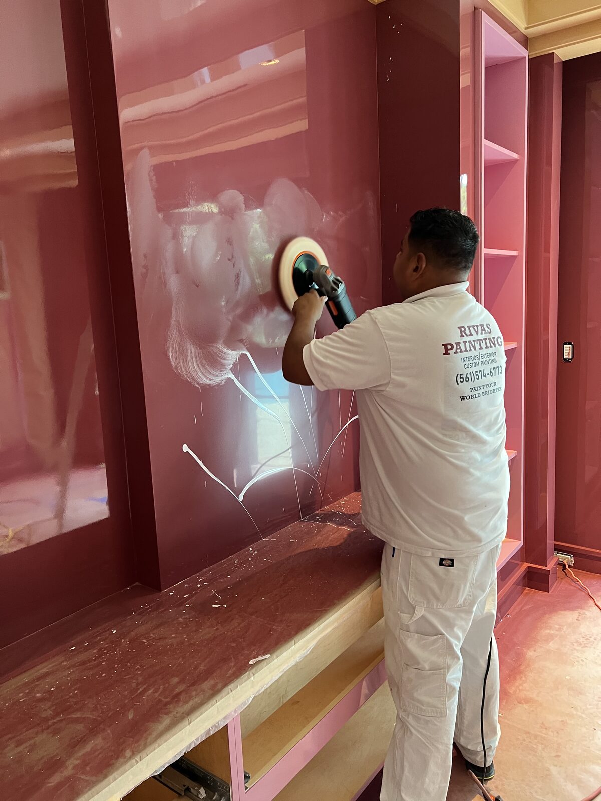 Painter buffing a deep red high-gloss lacquer wall to a mirror finish