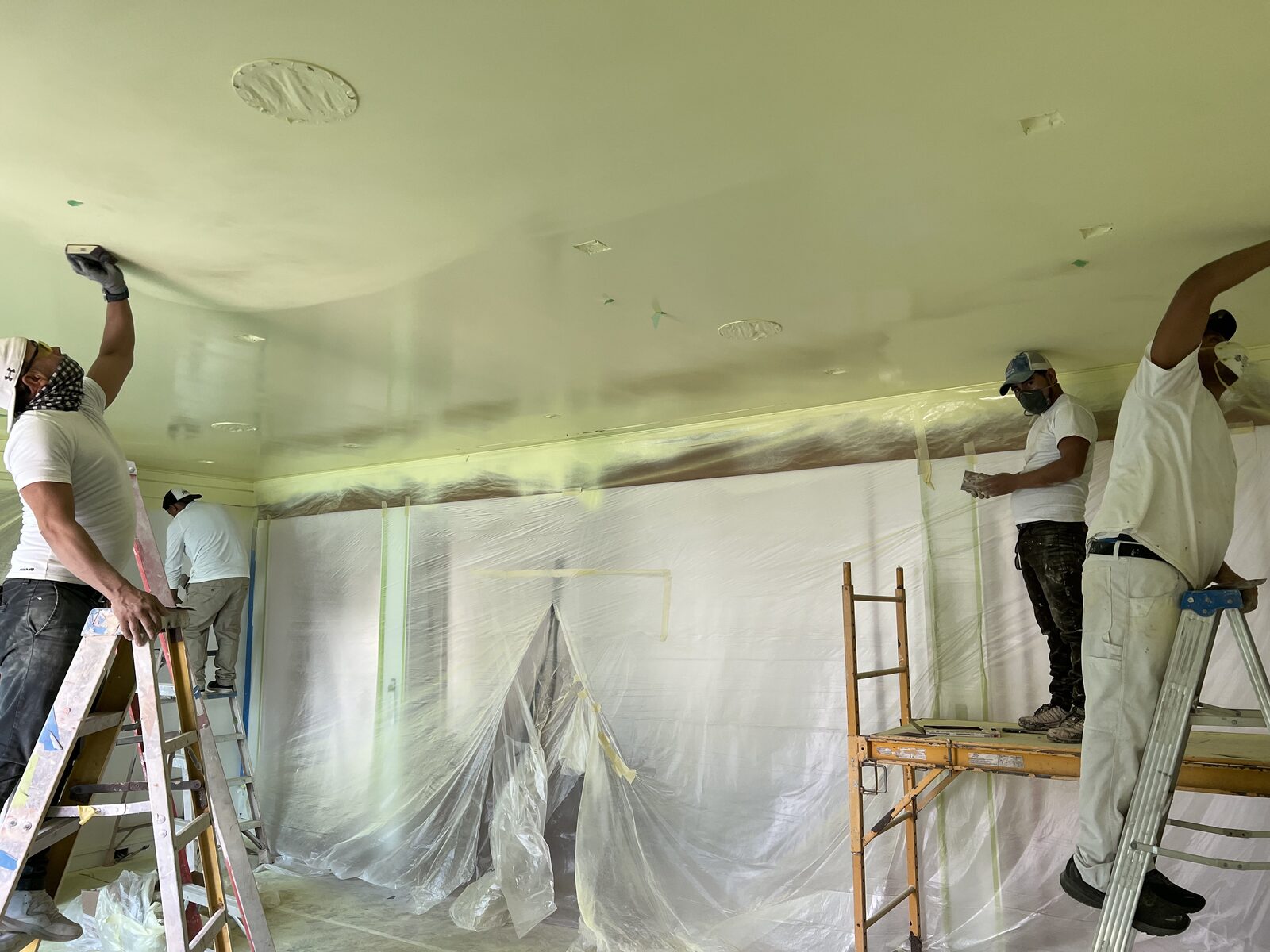 Four-man Rivas crew skim-coating a ceiling from ladders and scaffold