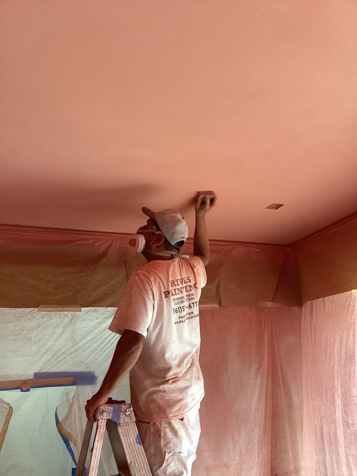 Rivas painter rolling coral ceiling coating over fully masked walls