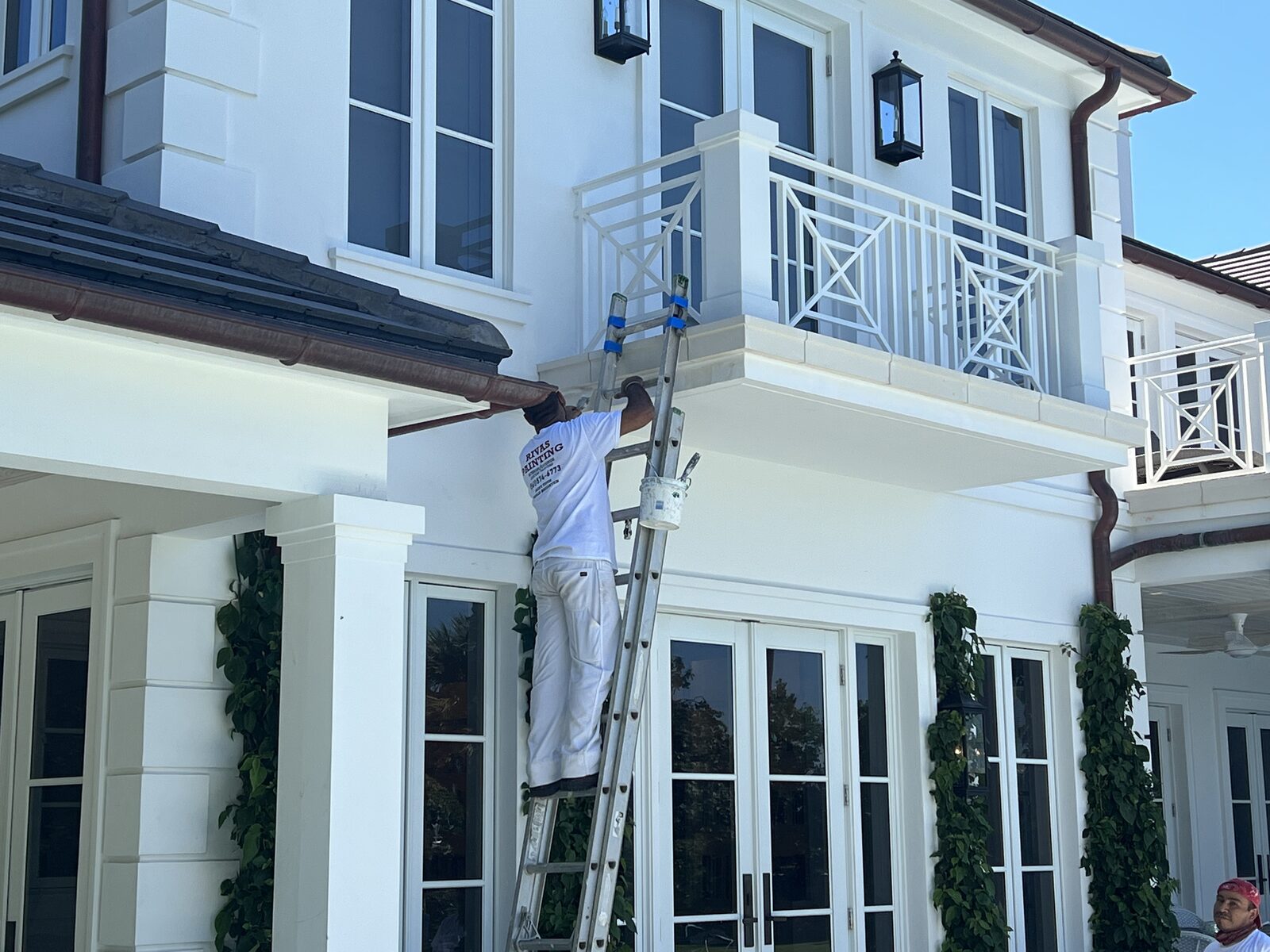 Rivas painter on an extension ladder cutting in exterior soffit and trim