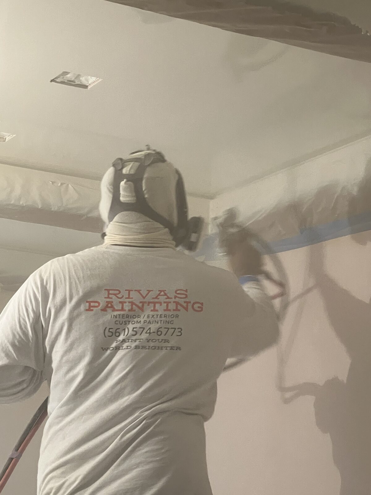 Rivas painter in a respirator spraying a masked interior ceiling