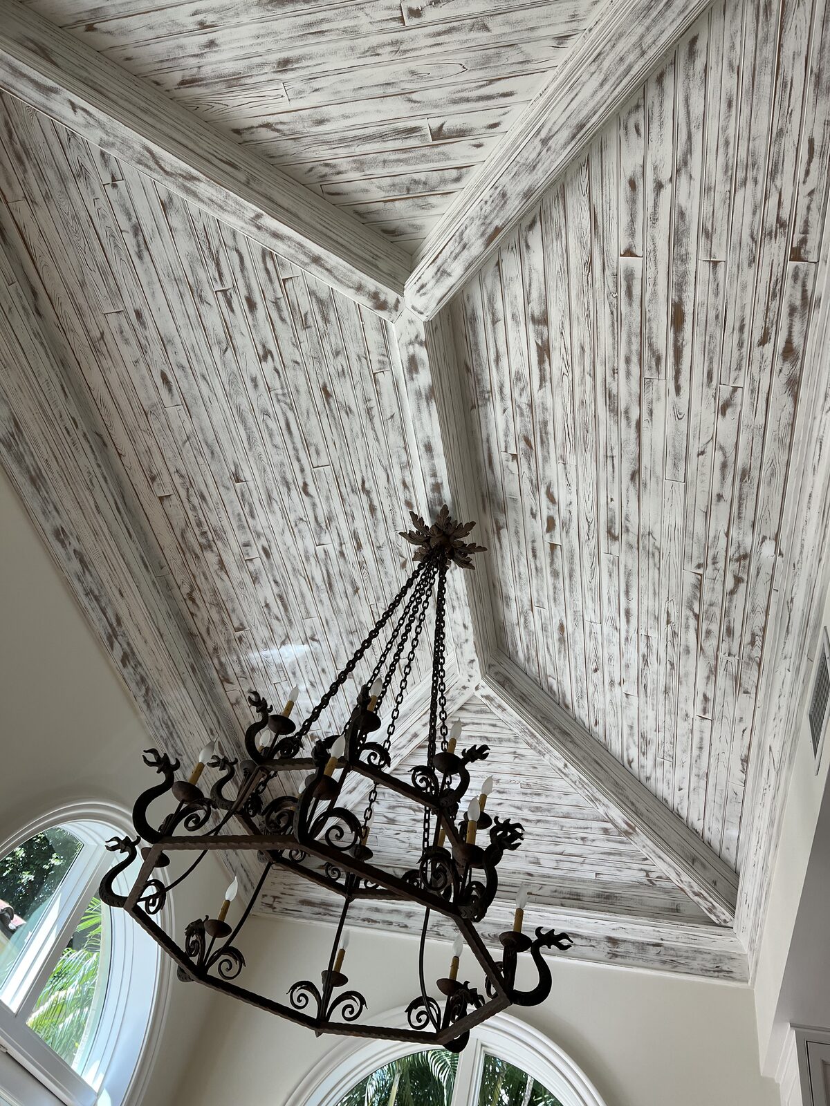Whitewashed distressed plank vaulted ceiling with wrought iron chandelier